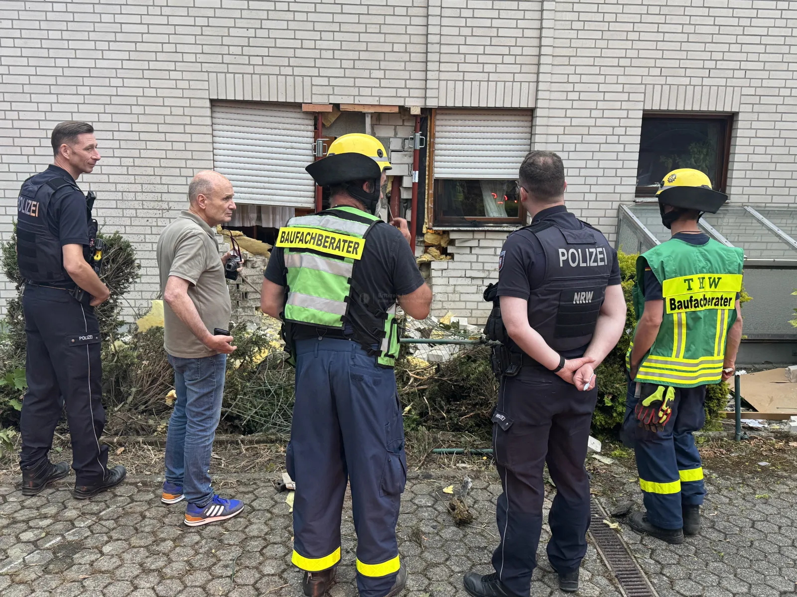 Einsatzkräfte begutachten beschädigte Hauswand nach Unfall