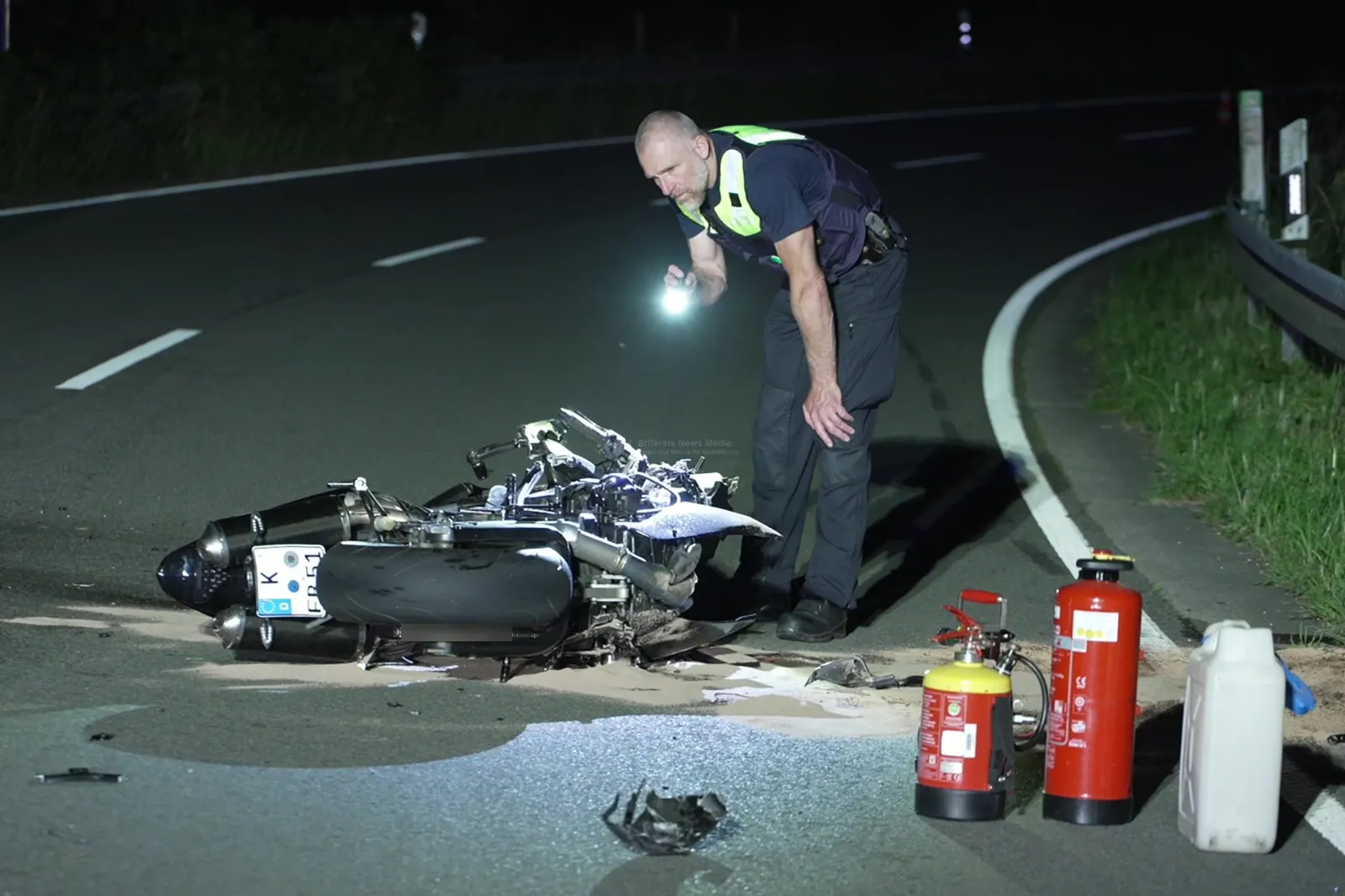 Motorrad nach Unfall liegt auf der Straße, Polizist untersucht Unfallstelle
