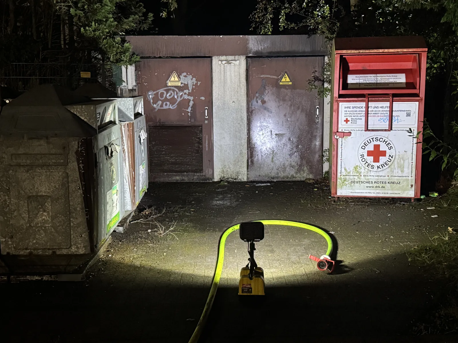 Beleuchtete Trafostationstür mit Kabel und DRK-Container bei Nacht