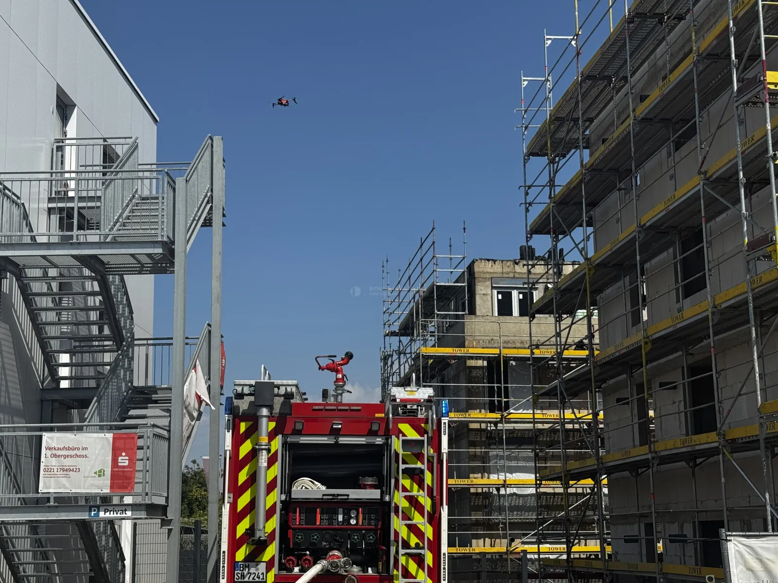 Feuerwehrfahrzeug vor Baustelle mit Drohne im Himmel