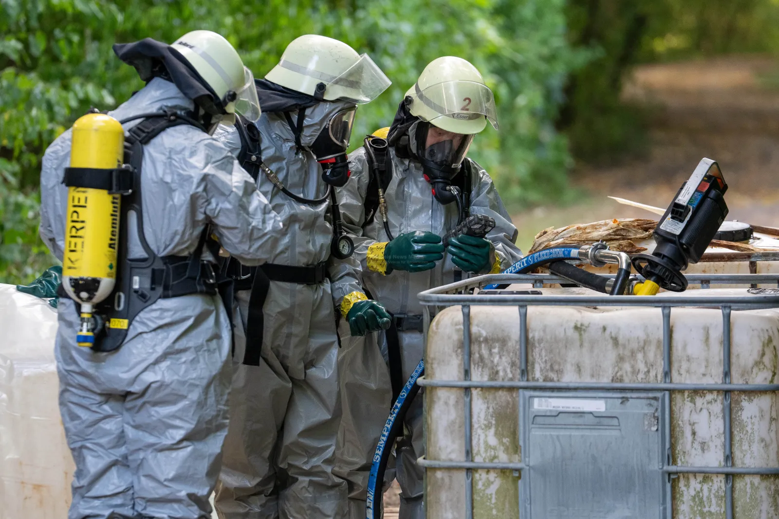 Feuerwehrleute in Schutzanzügen untersuchen Container mit unbekannter Flüssigkeit