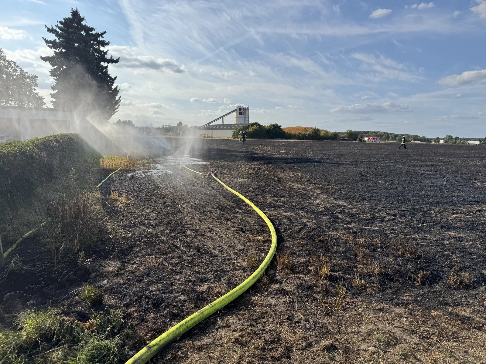 Gelöschtes Stoppelfeld nach Brand mit Feuerwehrschläuchen und Einsatzkräften